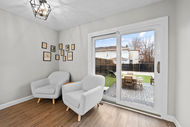 sitting room featuring a notable chandelier, a textured ceiling, baseboards, and wood finished floors