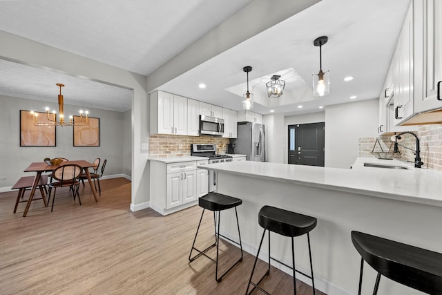 kitchen with stainless steel appliances, light countertops, a sink, light wood-type flooring, and a peninsula