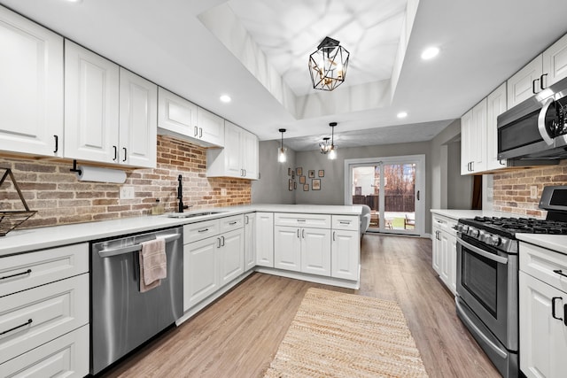 kitchen featuring stainless steel appliances, a peninsula, a sink, decorative backsplash, and a raised ceiling