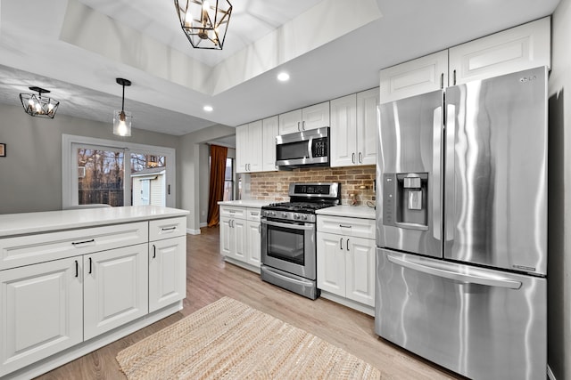 kitchen featuring a tray ceiling, light countertops, backsplash, light wood-style flooring, and appliances with stainless steel finishes