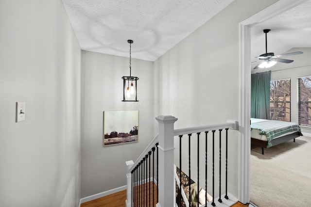 hallway with baseboards, a textured ceiling, and an upstairs landing