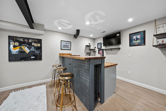 bar with a bar, recessed lighting, wood finished floors, and baseboards