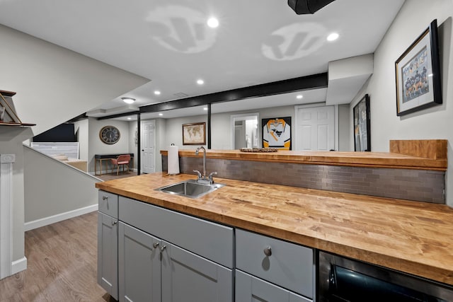 kitchen with butcher block counters, decorative backsplash, gray cabinetry, a sink, and wood finished floors