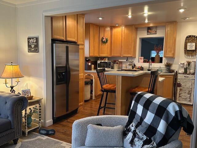 kitchen with a breakfast bar area, dark wood-style flooring, a center island, stainless steel appliances, and light countertops