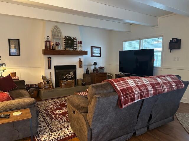 living room featuring a fireplace with raised hearth, beamed ceiling, and wood finished floors