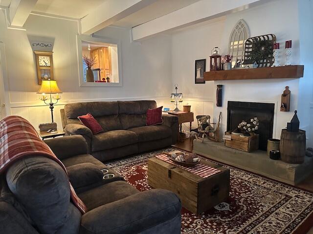 living area with a fireplace with raised hearth, wainscoting, beam ceiling, and a decorative wall