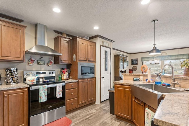 kitchen with light wood finished floors, stainless steel appliances, wall chimney range hood, pendant lighting, and a sink