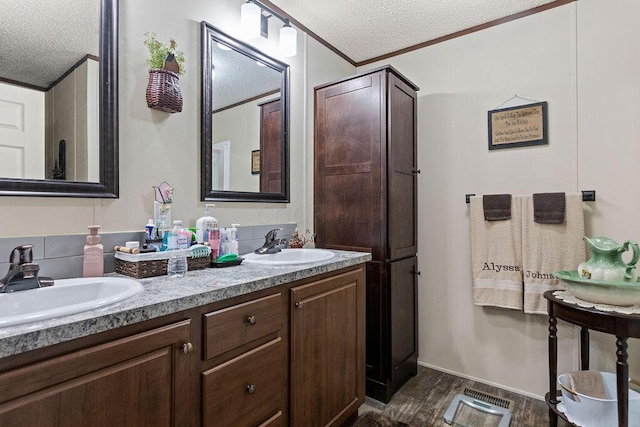 full bathroom with a textured ceiling, wood finished floors, a sink, and crown molding