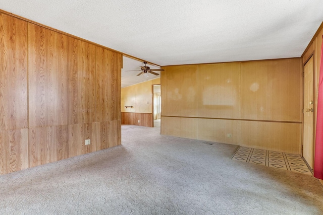 carpeted empty room featuring lofted ceiling, wood walls, a textured ceiling, and ceiling fan