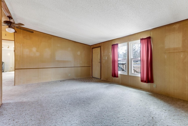 carpeted spare room featuring ceiling fan, wooden walls, and a textured ceiling