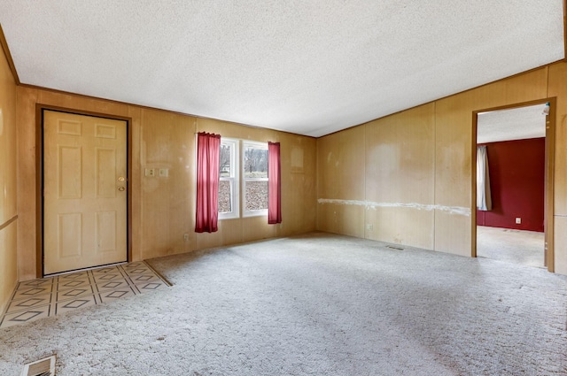 carpeted empty room with visible vents, wood walls, and a textured ceiling