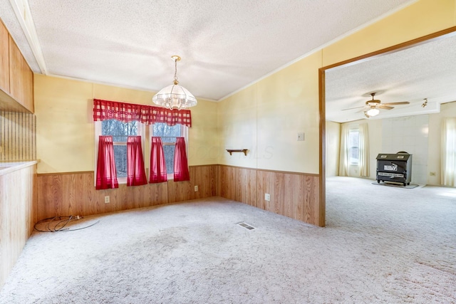 empty room with carpet floors, visible vents, wainscoting, wood walls, and a textured ceiling