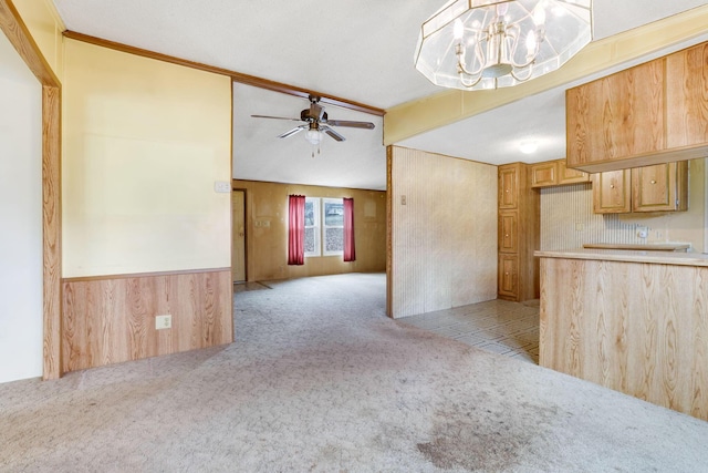 kitchen featuring a wainscoted wall, light colored carpet, vaulted ceiling, wood walls, and ceiling fan with notable chandelier