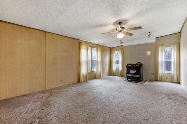 unfurnished living room featuring a wood stove, wood walls, carpet, and a textured ceiling