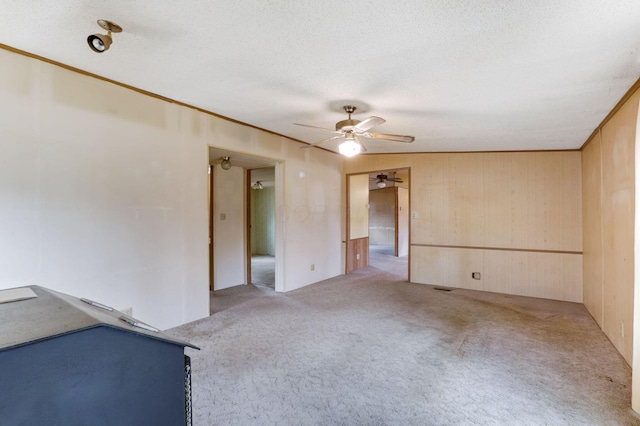 spare room with crown molding, light carpet, ceiling fan, wooden walls, and a textured ceiling