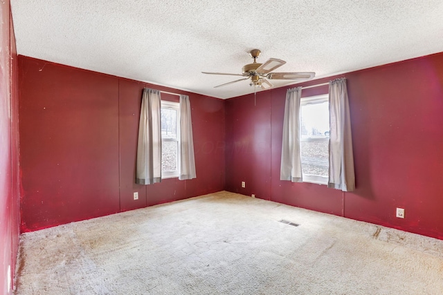 carpeted empty room featuring a textured ceiling, ceiling fan, a wealth of natural light, and visible vents