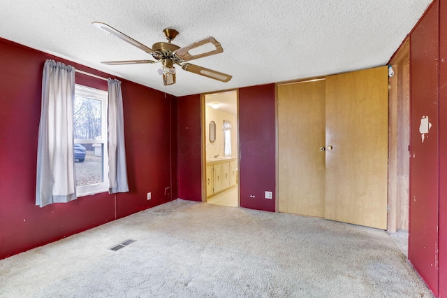 unfurnished bedroom with visible vents, connected bathroom, a textured ceiling, and carpet flooring