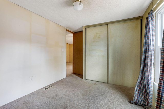 unfurnished bedroom with carpet floors, a closet, visible vents, and a textured ceiling