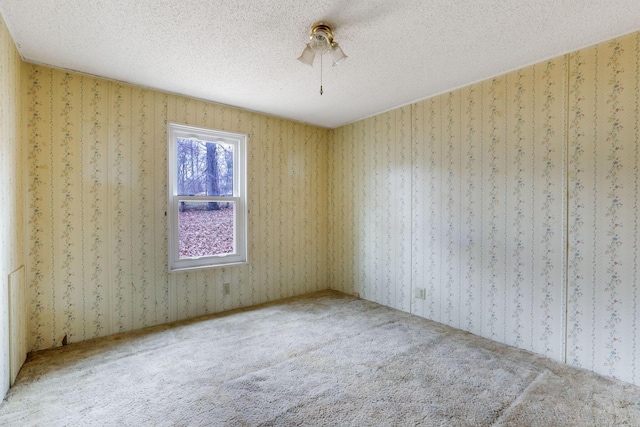 spare room with carpet floors, a textured ceiling, and wallpapered walls