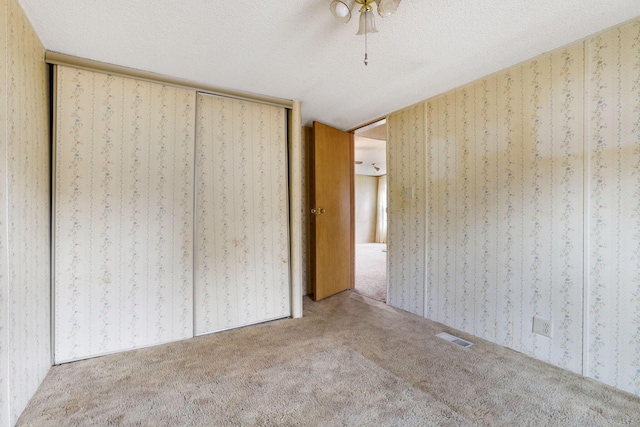 unfurnished bedroom featuring wallpapered walls, a textured ceiling, and carpet flooring