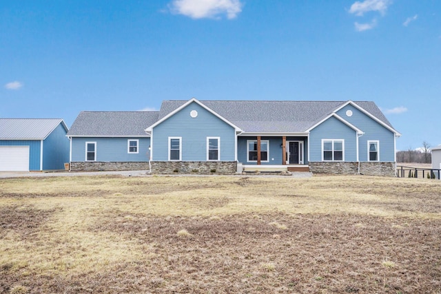 single story home with stone siding, a front lawn, covered porch, and an outdoor structure