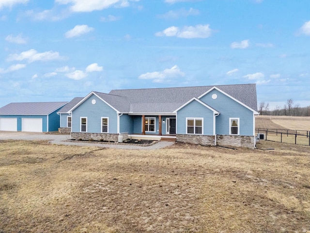 ranch-style house with an outdoor structure, covered porch, fence, and stone siding