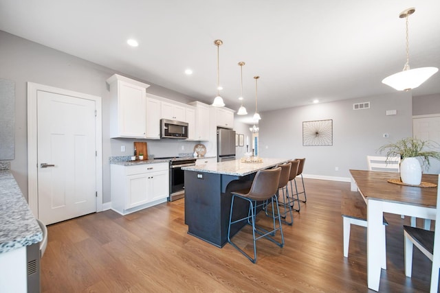 kitchen with visible vents, a center island, appliances with stainless steel finishes, wood finished floors, and white cabinetry