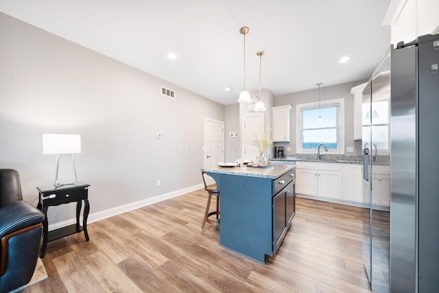 kitchen featuring visible vents, stainless steel fridge, a breakfast bar area, and white cabinets