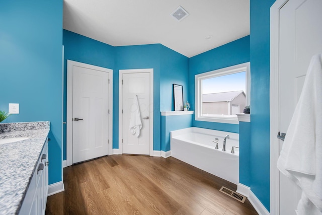 full bath with vanity, a garden tub, wood finished floors, and visible vents