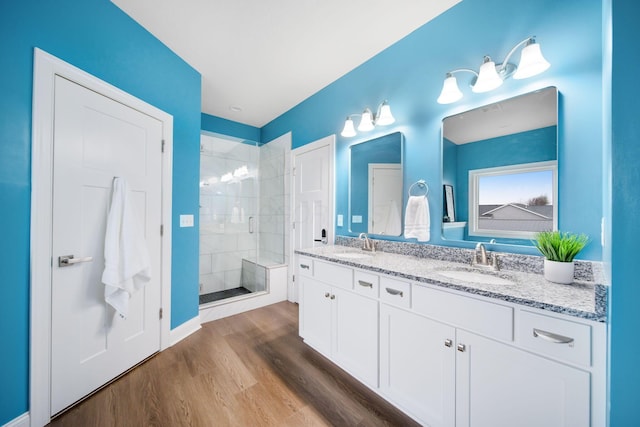 bathroom featuring a sink, wood finished floors, a stall shower, and double vanity