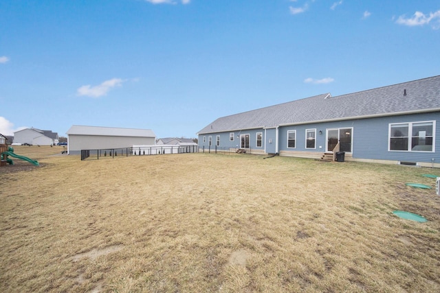 back of property with an outdoor structure, a playground, and a yard