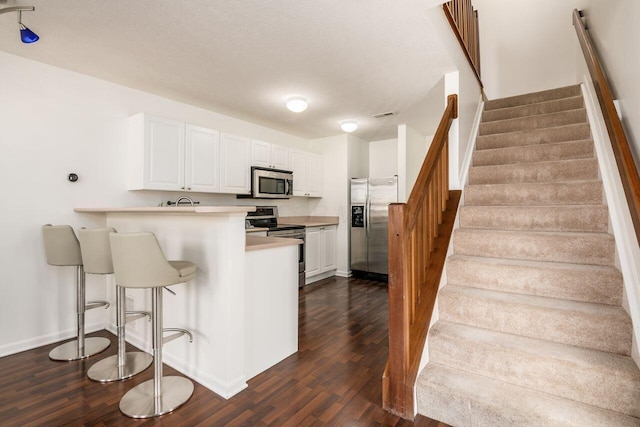 kitchen featuring white cabinets, a peninsula, stainless steel appliances, and dark wood-type flooring