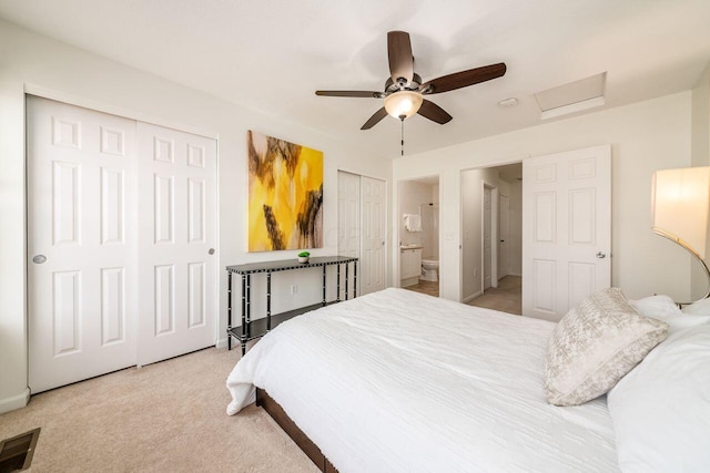 carpeted bedroom with visible vents, ceiling fan, multiple closets, attic access, and ensuite bath