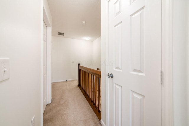 hall with visible vents, an upstairs landing, and light colored carpet