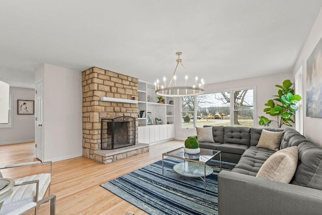 living area featuring baseboards, a fireplace, an inviting chandelier, and wood finished floors