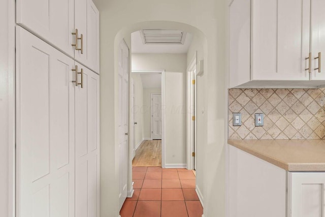 hallway featuring light tile patterned floors, baseboards, and arched walkways