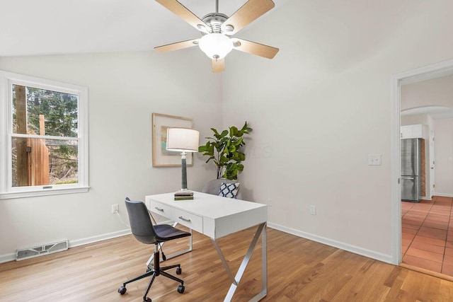 office space featuring lofted ceiling, arched walkways, visible vents, baseboards, and light wood finished floors