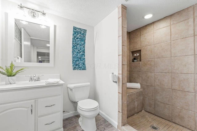 full bath featuring toilet, a textured ceiling, vanity, tiled shower, and baseboards