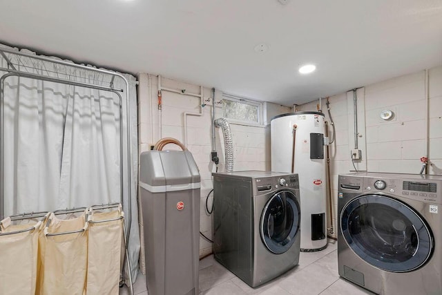 clothes washing area featuring concrete block wall, light tile patterned floors, electric water heater, washer and dryer, and laundry area