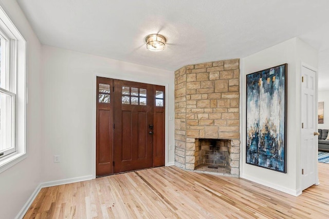 foyer entrance featuring a healthy amount of sunlight, a fireplace, baseboards, and wood finished floors