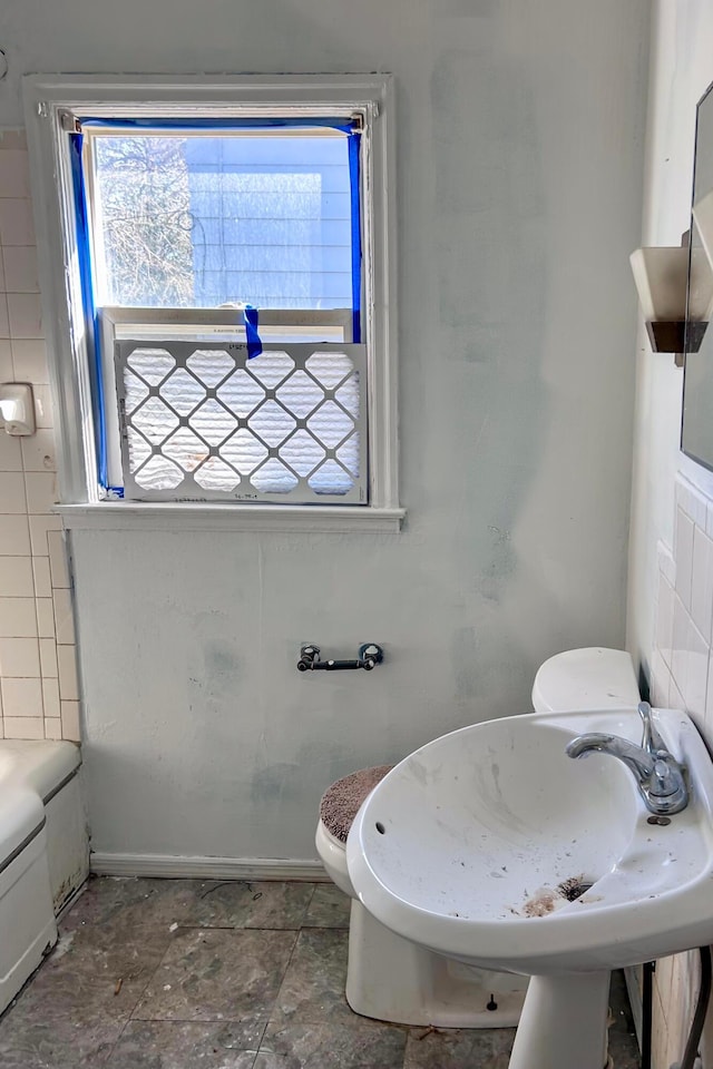 bathroom with a bath, toilet, and baseboards