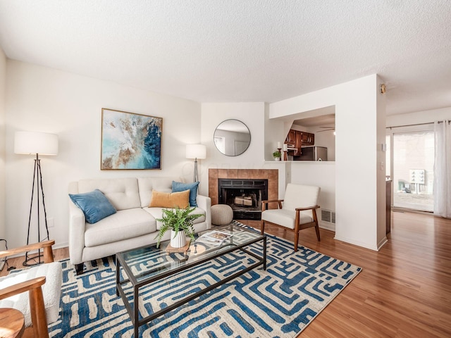 living room with baseboards, visible vents, a tile fireplace, wood finished floors, and a textured ceiling