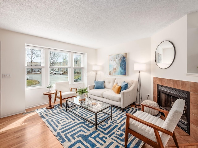 living room with a tile fireplace, a textured ceiling, baseboards, and wood finished floors