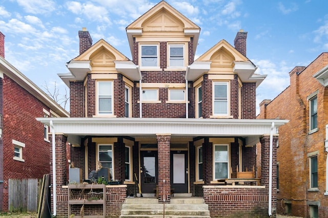 view of front of home featuring covered porch, brick siding, and a chimney