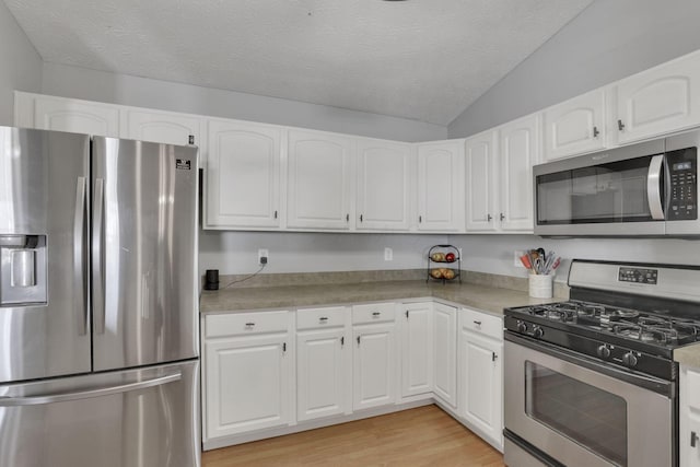 kitchen featuring appliances with stainless steel finishes, white cabinets, vaulted ceiling, a textured ceiling, and light wood-type flooring