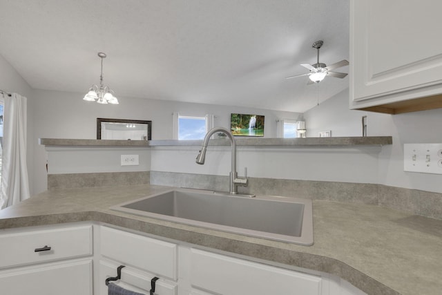 kitchen with white cabinets, lofted ceiling, pendant lighting, a sink, and ceiling fan with notable chandelier