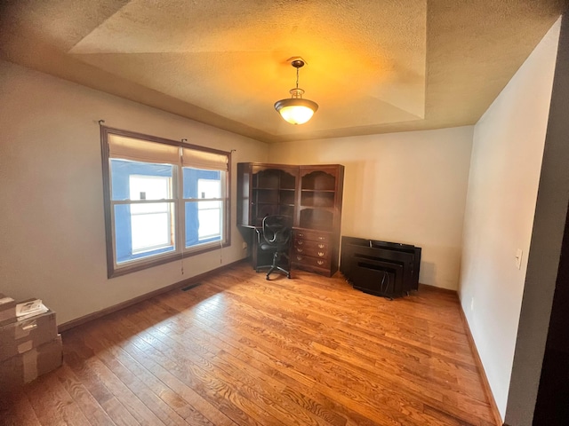 unfurnished office featuring baseboards, a textured ceiling, and hardwood / wood-style floors