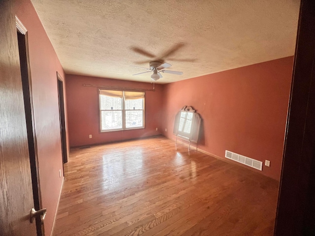 empty room featuring light wood-style floors, ceiling fan, visible vents, and a textured ceiling