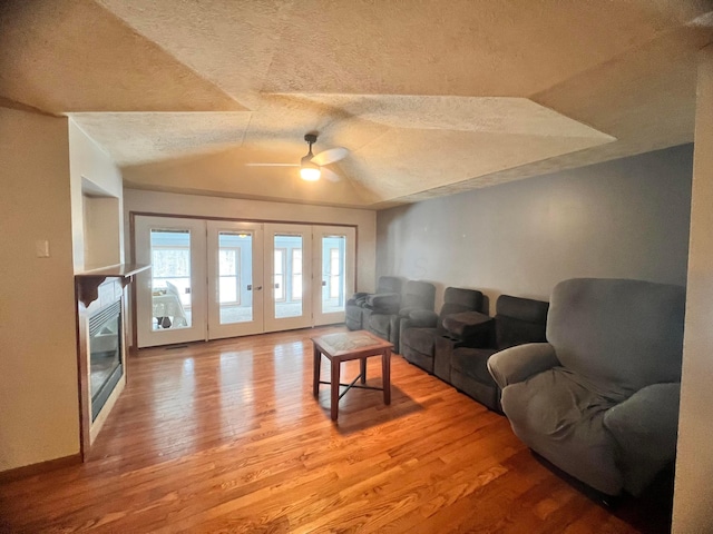 living area featuring french doors, lofted ceiling, ceiling fan, a textured ceiling, and wood finished floors