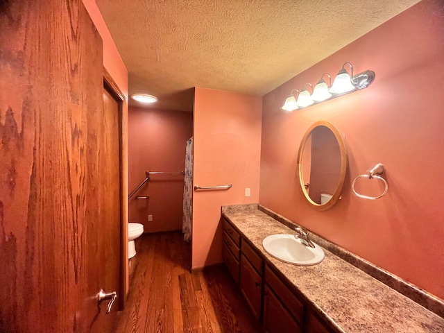 full bath featuring a textured ceiling, vanity, wood finished floors, and toilet